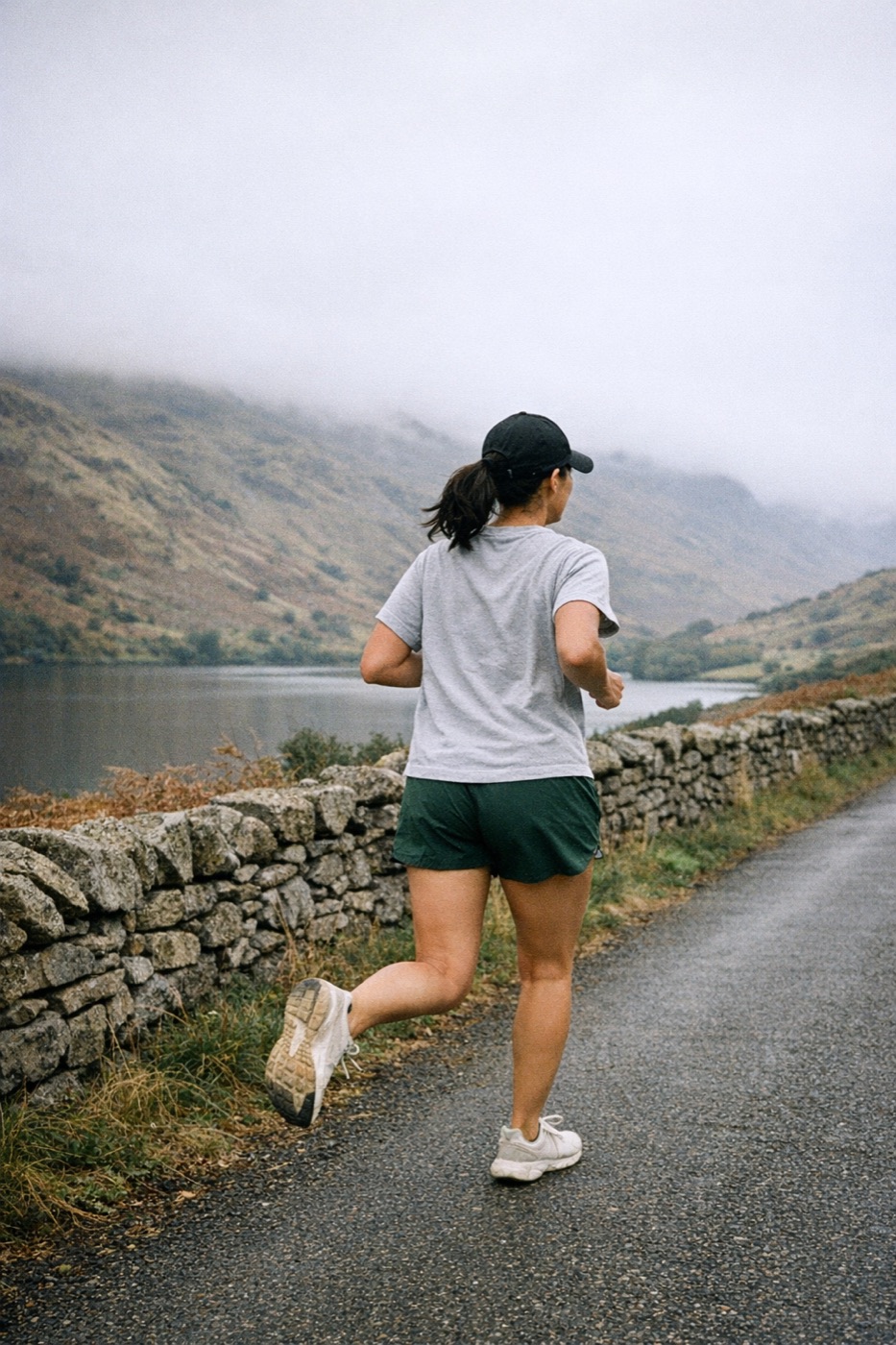 Woman running along a misty Lake District road beside a dry-stone wall